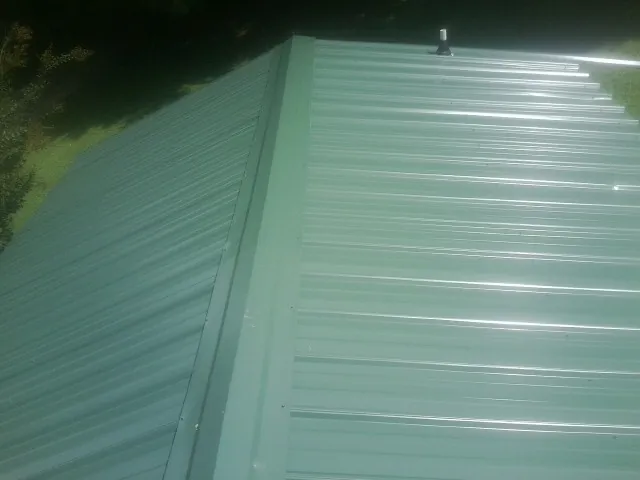 New green metal panels meeting at the ridge of a roof — Flat Roof Repair work by our crew in Newark
