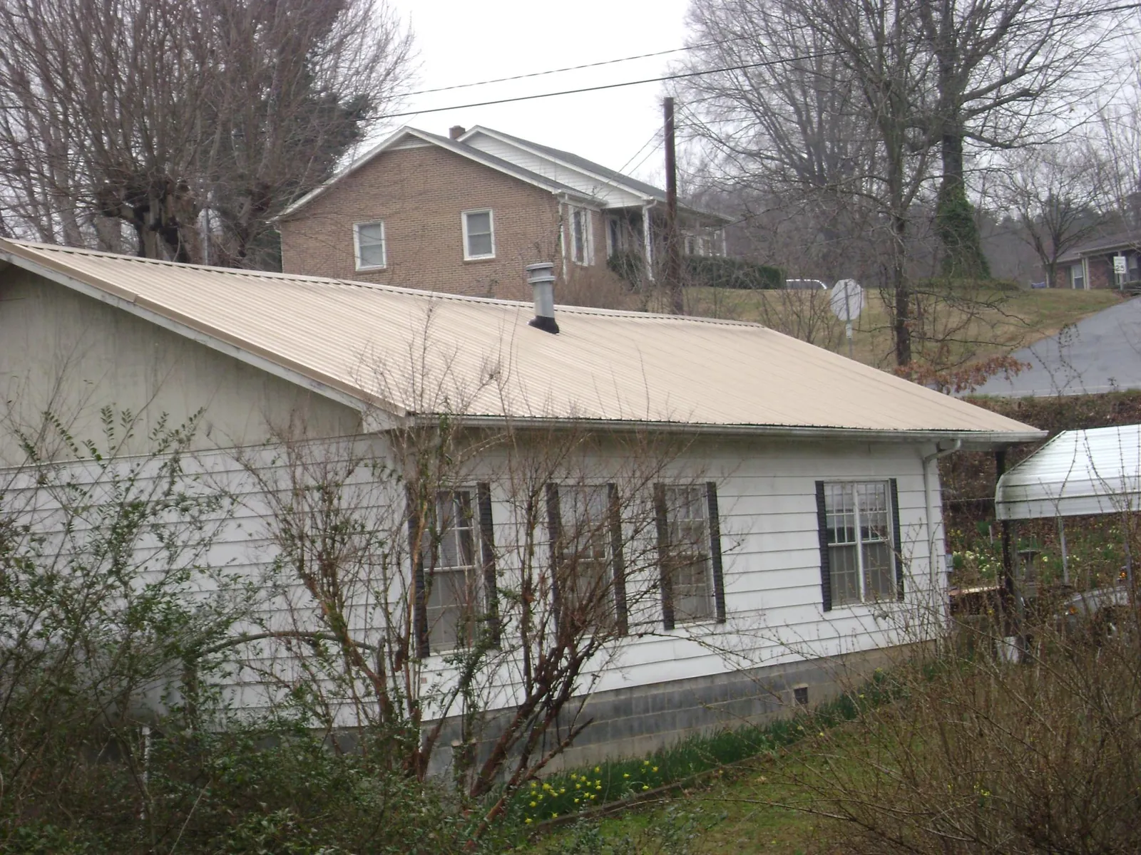 Tan metal roof on a white sided house set into a hillside — Commercial Roofing by Roofing Brothers in Newark